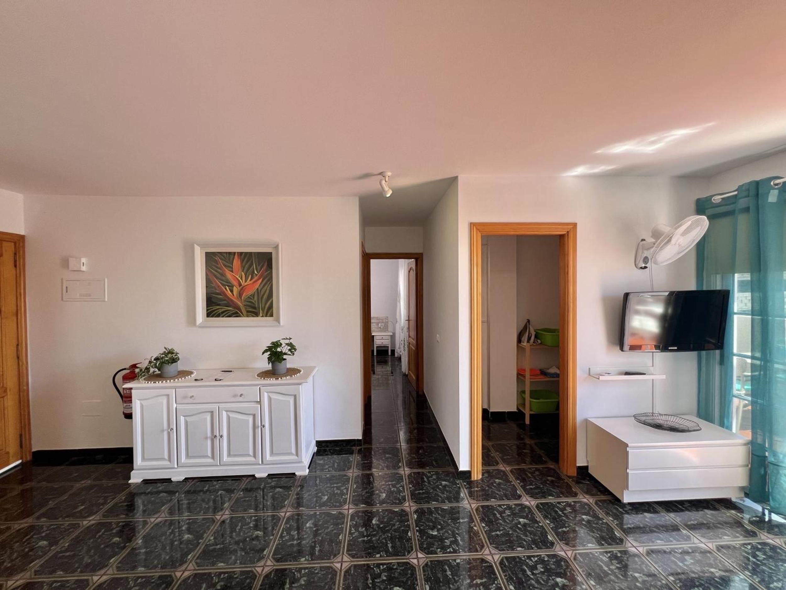 A hallway with a white cabinet, a painting, and a TV on a stand.