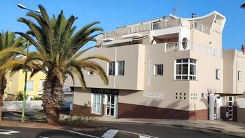Un edificio de varios pisos con un cartel que dice 'FUEGO NUEVO' en la planta baja, un balcón en el nivel superior y una palmera en primer plano.