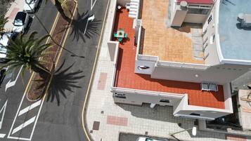 Luchtbeeld van een gebouw met een rood pannendak, een parkeerplaats met meerdere auto's en palmbomen.