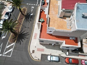 Vista aèria d'un edifici amb teulada vermella, un aparcament amb diversos cotxes i palmeres.