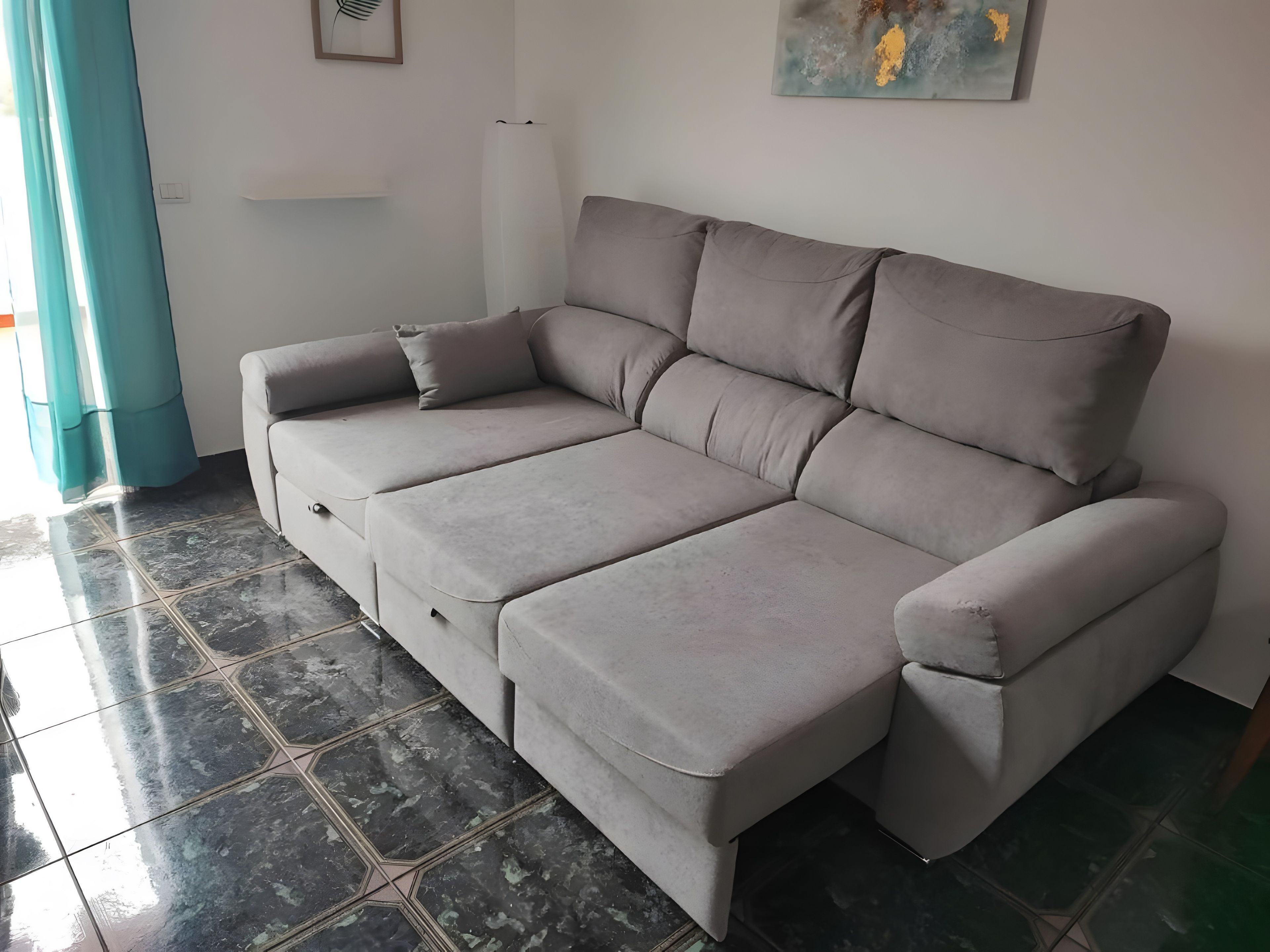 A grey sofa with a footrest, a wall-mounted light, and a painting.