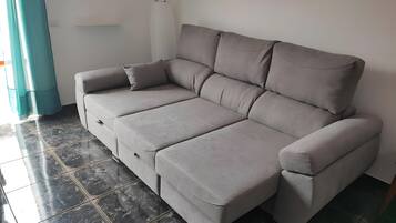 A grey sofa with a footrest, a wall-mounted light, and a painting.