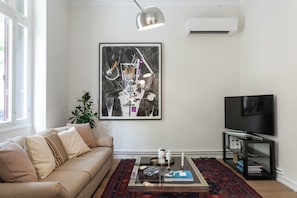 A living room with a sofa, a coffee table with decorative items, a flat-screen TV, and a large abstract painting on the wall. - One of Greece’s Most Extraordinary Homes (Athina)