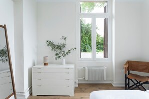 A bedroom with a white dresser, a plant, a window with shutters, a radiator, and a chair. - One of Greece’s Most Extraordinary Homes (Athina)