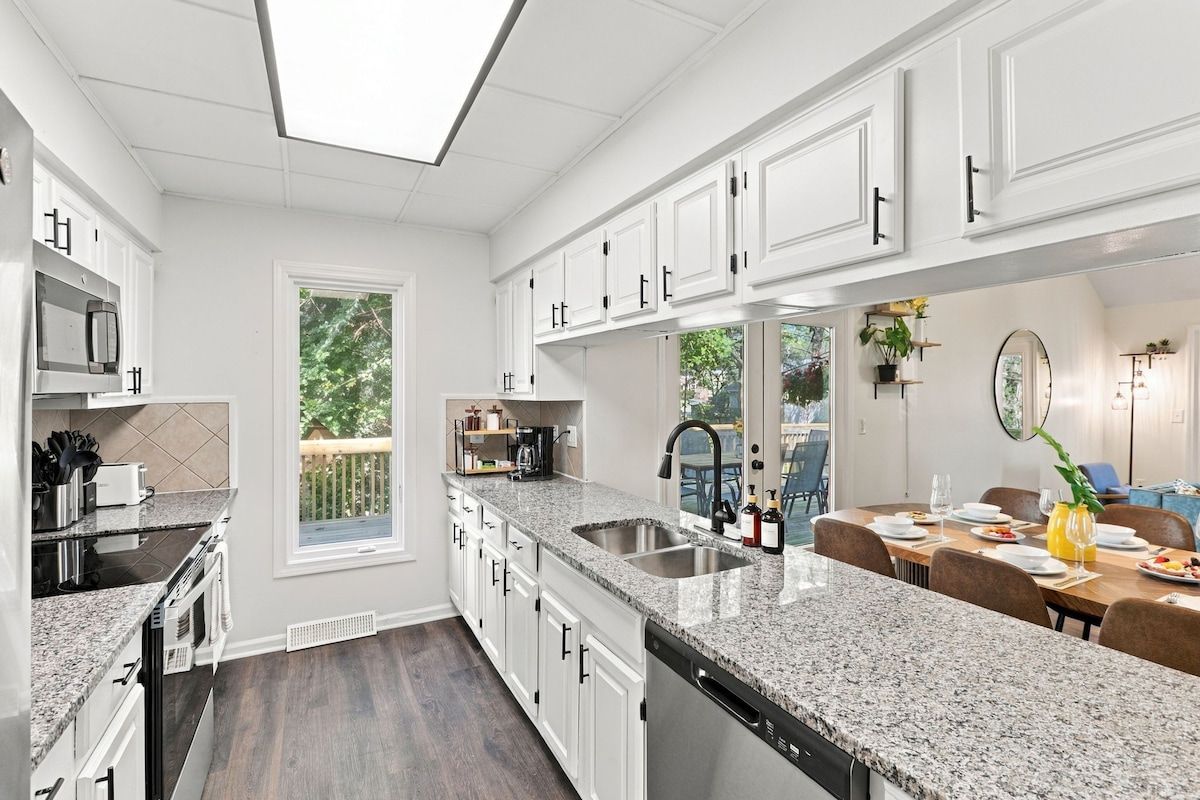 A modern kitchen with white cabinetry, granite countertops, and a large window.