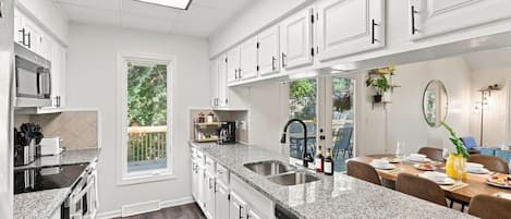 A modern kitchen with white cabinetry, granite countertops, and a large window.