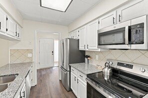 A modern kitchen with white cabinets, a stainless steel refrigerator, a microwave, and a gas stove. - Cbus Hub · 2 Kings + Loft  2 twin beds · Sleeps 6 · Private Deck & Grill (Columbus)