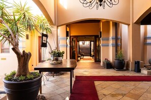 A hotel lobby with a grand staircase, potted plants, and a red carpet. - Anta Boga Hotel (Bloemfontein)