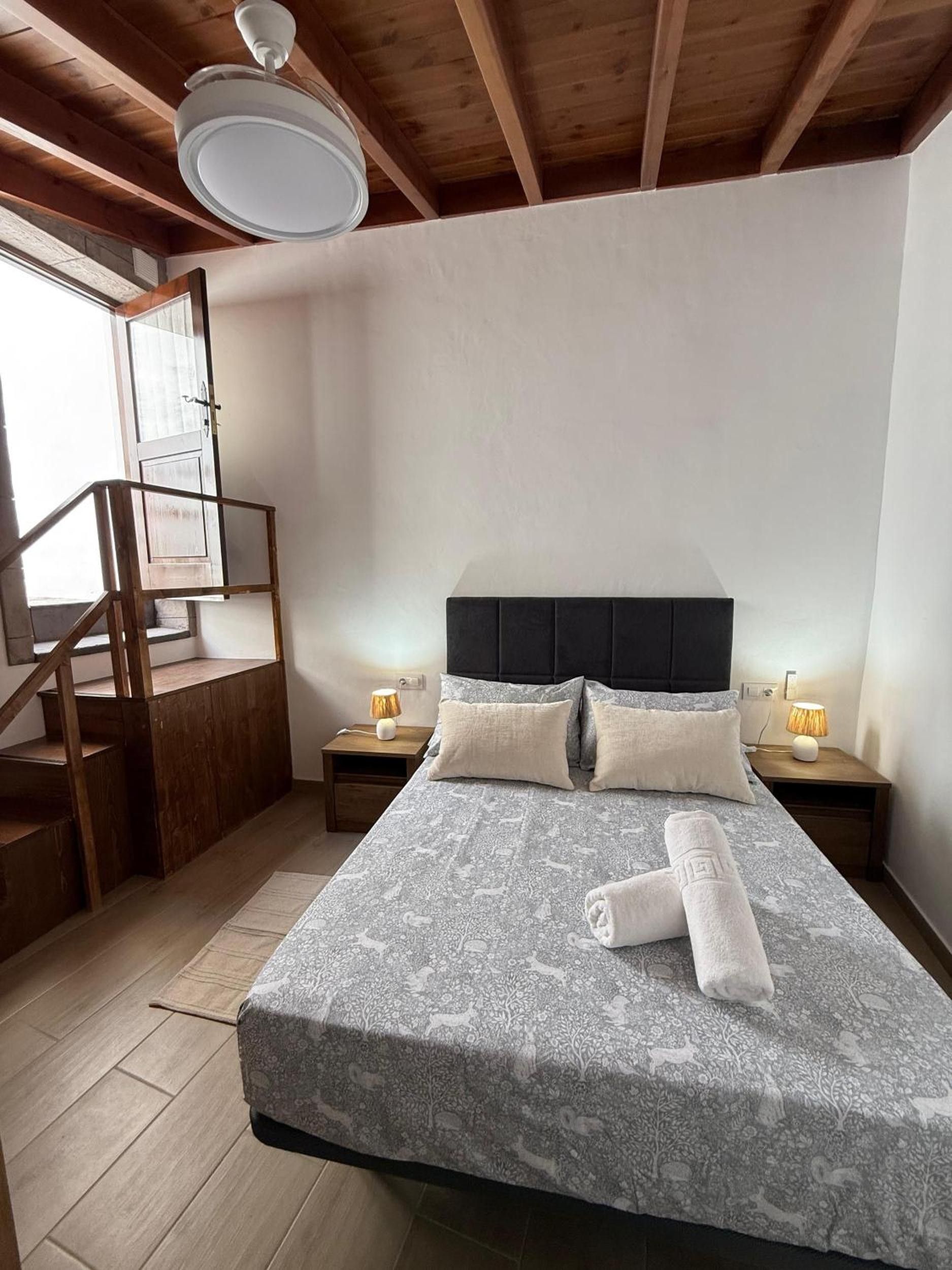 Un dormitorio con cama, mesitas de noche, una escalera de madera y un ventilador de techo.