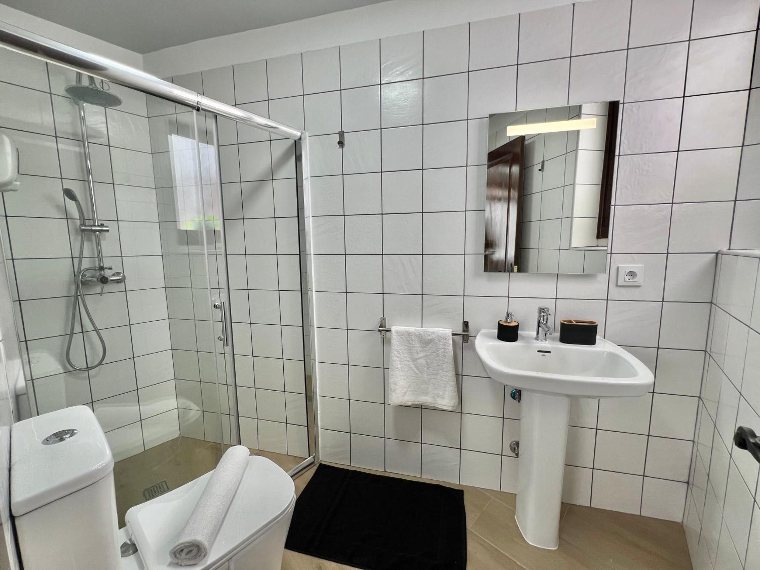 Een badkamer met een douchecabine van glas, een wit wastafeltje en een spiegel erboven.