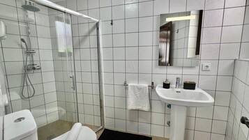 Een badkamer met een douchecabine van glas, een wit wastafeltje en een spiegel erboven.