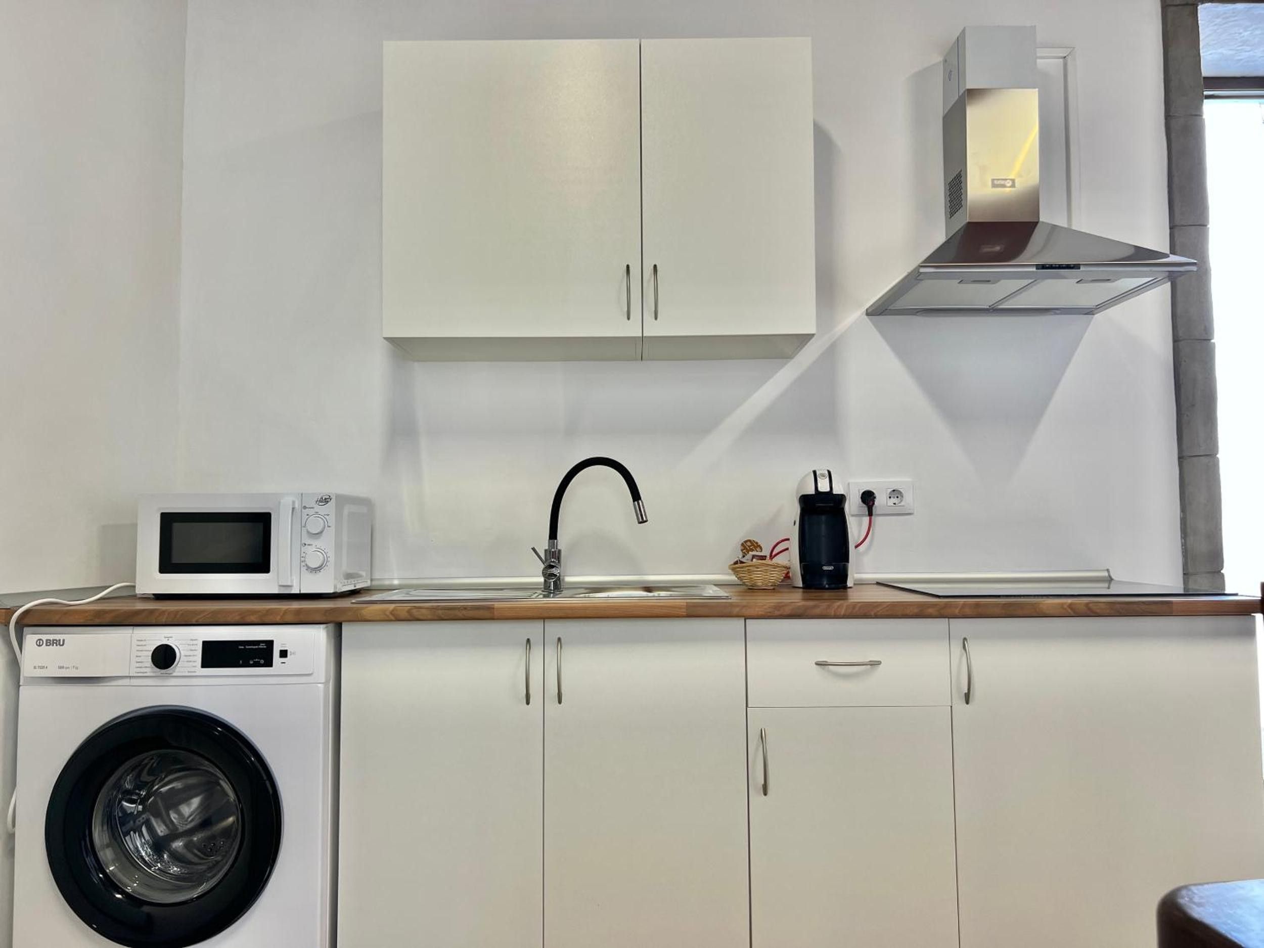 A compact kitchen with a washing machine, microwave, sink, and a coffee maker.