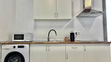 A compact kitchen with a washing machine, microwave, sink, and a coffee maker.