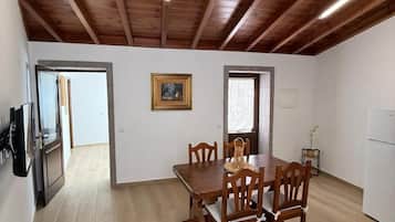 Een eetgedeelte met een houten tafel en stoelen, een schilderij aan de muur, en een keuken met een koelkast.