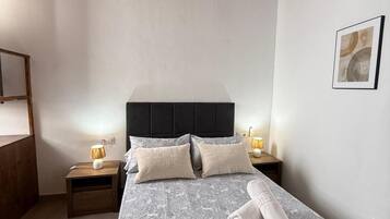 Un dormitorio con una cama, mesitas de noche, una lámpara, un cuadro enmarcado en la pared y techo de madera.