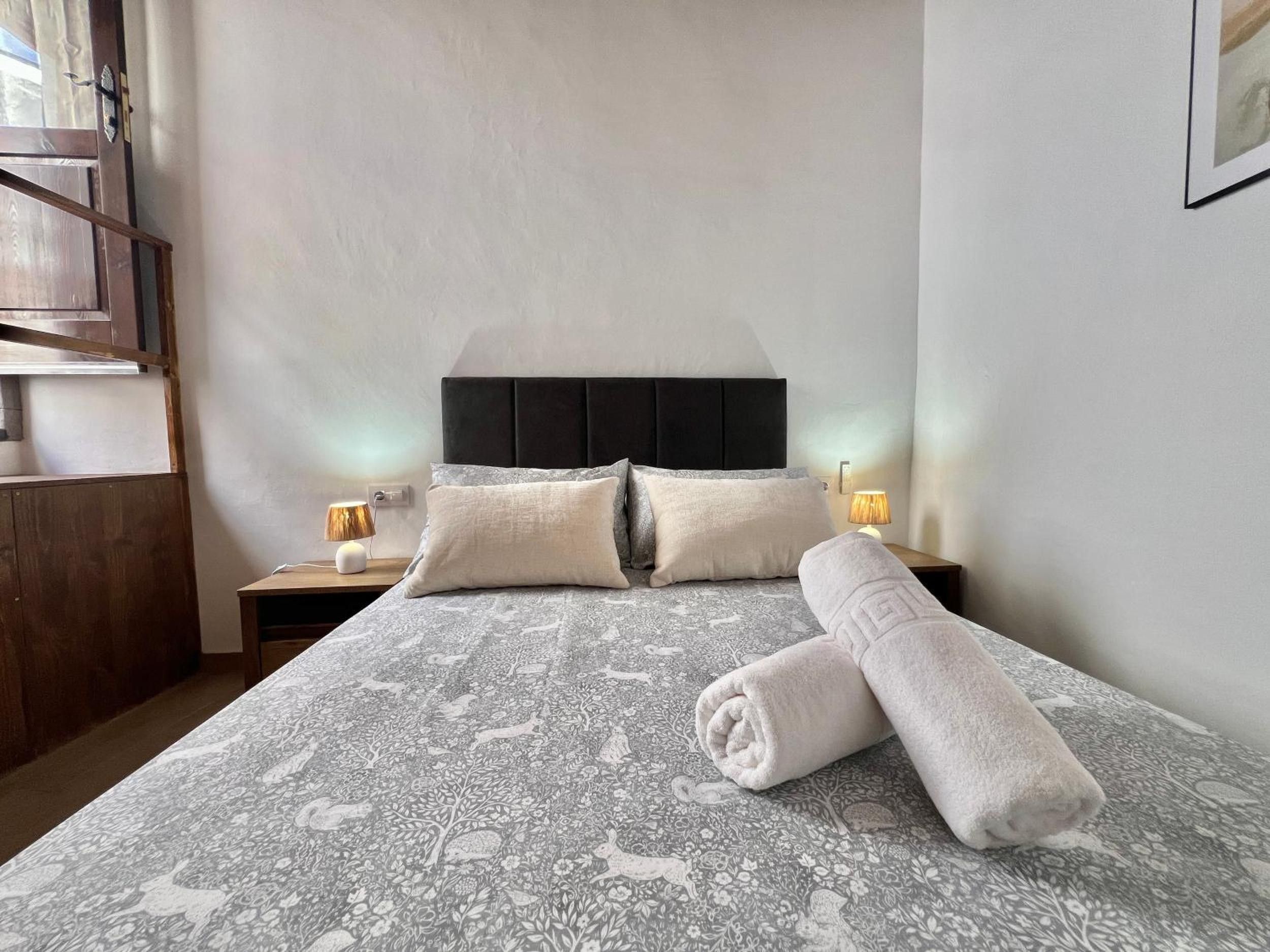A hotel room with a bed, two bedside tables, a headboard, and a rolled towel on the bed.