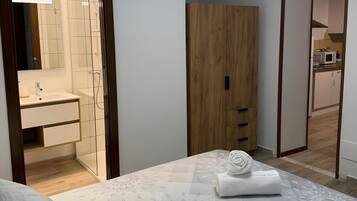 Een slaapkamer met een bed, een houten garderobe, een badkamer met een spiegel en wastafel, en een keuken die zichtbaar is door een open deur.