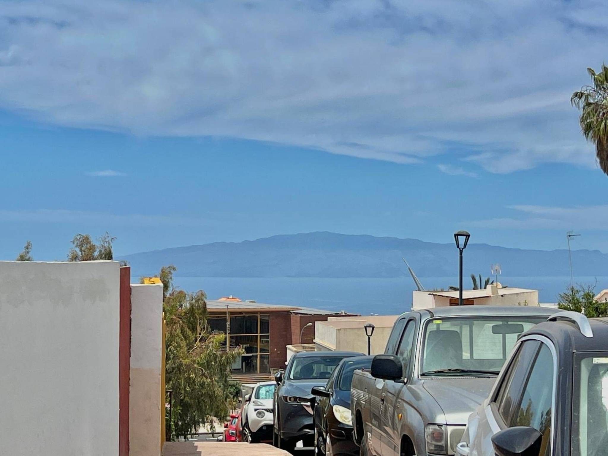 Un estacionamiento con varios coches, edificios y montañas al fondo.