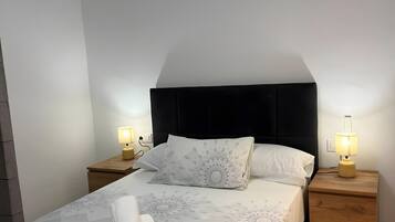 Una cama bien hecha con una colcha estampada, dos lámparas de noche y una mesita de noche de madera.