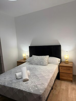 Una cama bien hecha con una colcha estampada, dos lámparas de noche y una mesita de noche de madera.