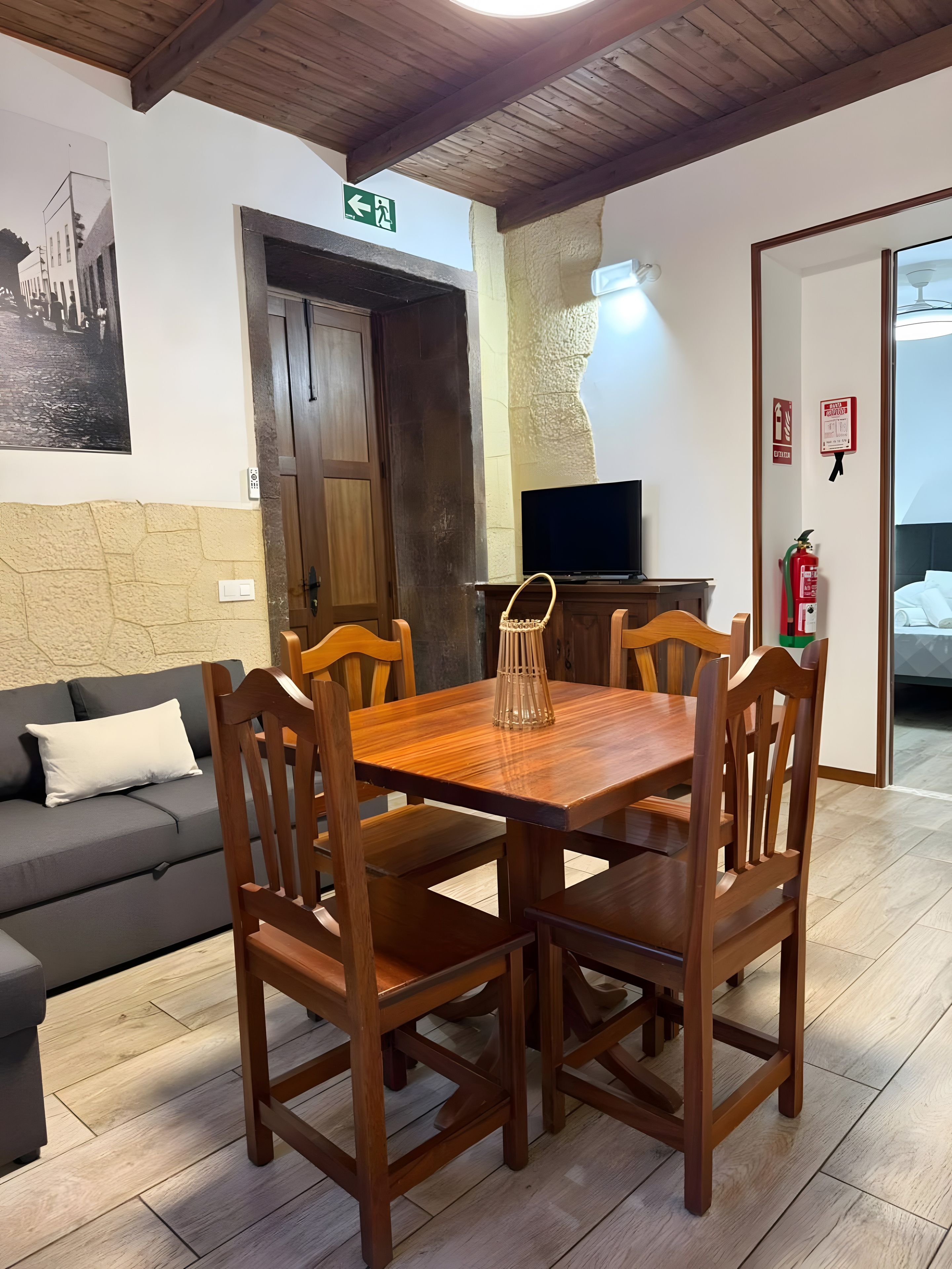 Een zithoek met een houten tafel en stoelen, een bank, een televisie en een brandblusser.