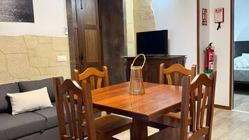Een zithoek met een houten tafel en stoelen, een bank, een televisie en een brandblusser.