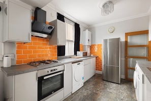 Eine kleine Küche mit Gasherd, Backofen, Waschmaschine und einem Edelstahl-Kühlschrank.