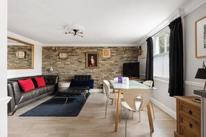 Ein modernes Wohnzimmer mit einer Steinwand, einem Sofa, einem Esstisch mit Stühlen und einem Fernseher.