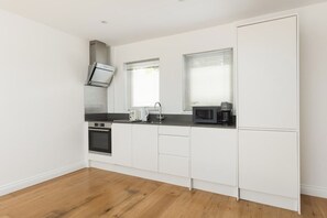A modern kitchen with white cabinetry, a built-in oven, a microwave, and a coffee maker. - New! Bright 2BR Flat w/Private Garden (Greater London)