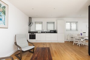 A modern kitchen with white cabinetry, a dining area with white chairs, and a wooden floor. - New! Bright 2BR Flat w/Private Garden (Greater London)
