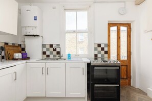 Eine Küche mit weißen Schränken, einem eingebauten Backofen, einem Fenster und einer Tür zum Garten.