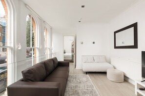 A modern living room with a brown sofa, a white couch, and a television on a white stand. - New! Stylish 3BR Mews House in Maida Vale (Greater London)