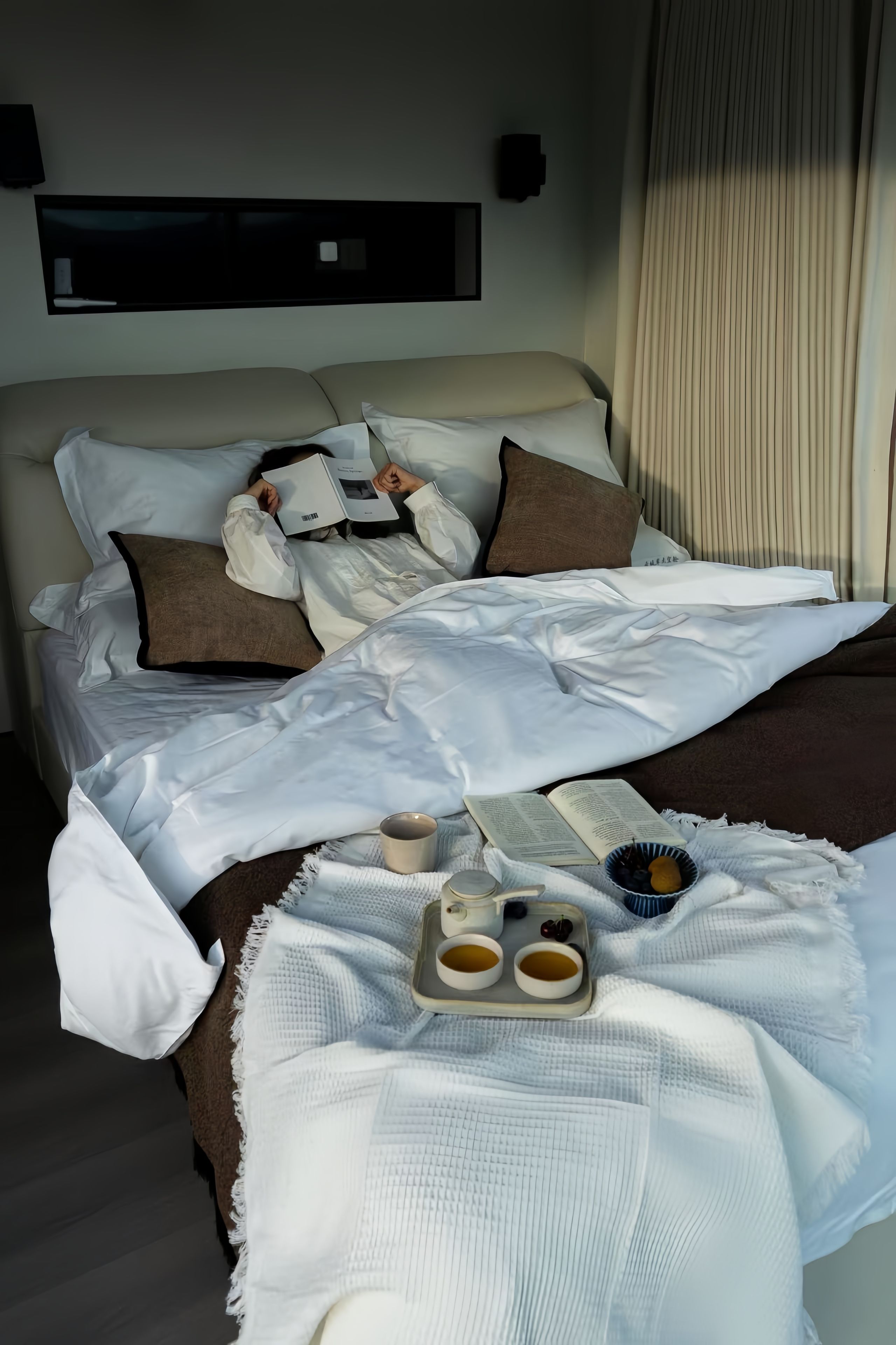 Et hotelværelse med en seng, puder, et bakke med kopper og en tepotte, samt et tæppe.