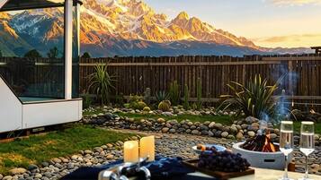 Een terras met een vuurkorf, kaarsen en een gedekte tafel, met uitzicht op een bergachtig landschap.