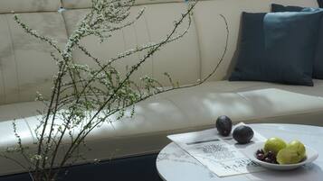A modern living room with a sofa, a coffee table with fruits and avocados, and a vase with branches.