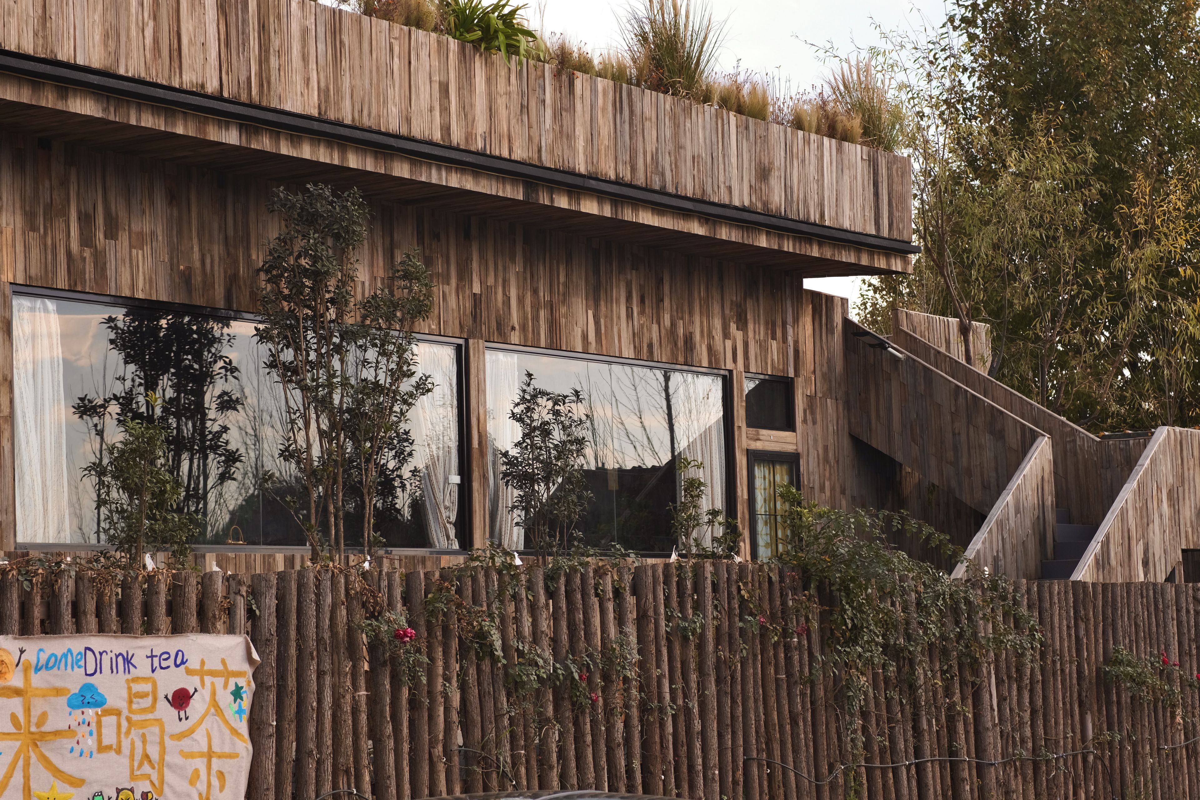 Un edificio moderno con fachada de madera, ventanas amplias y cerca de madera con plantas.
