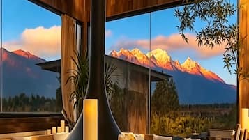 A modern interior with a sofa set, candles, and a large window with a mountain view.