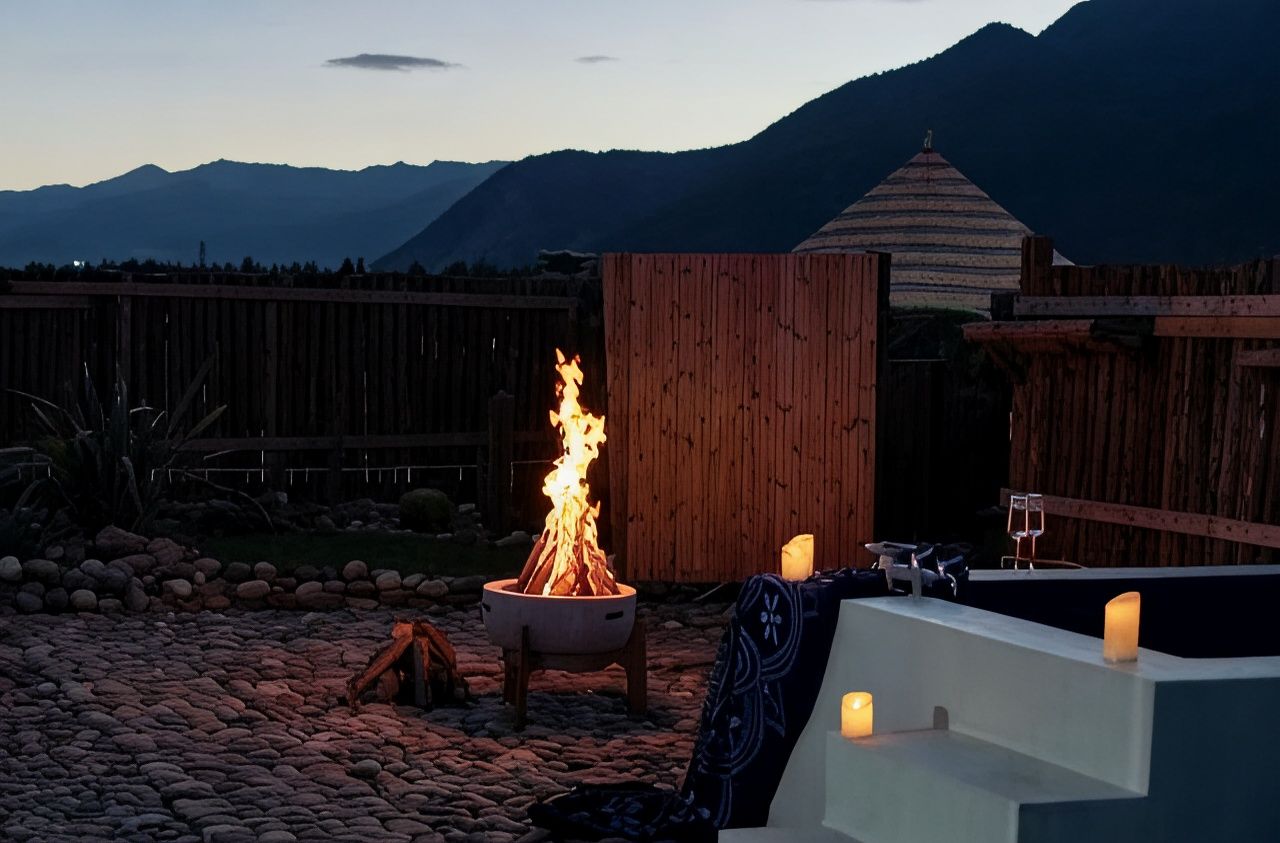 A fire pit with flames, a wooden fence, and a mountain backdrop.