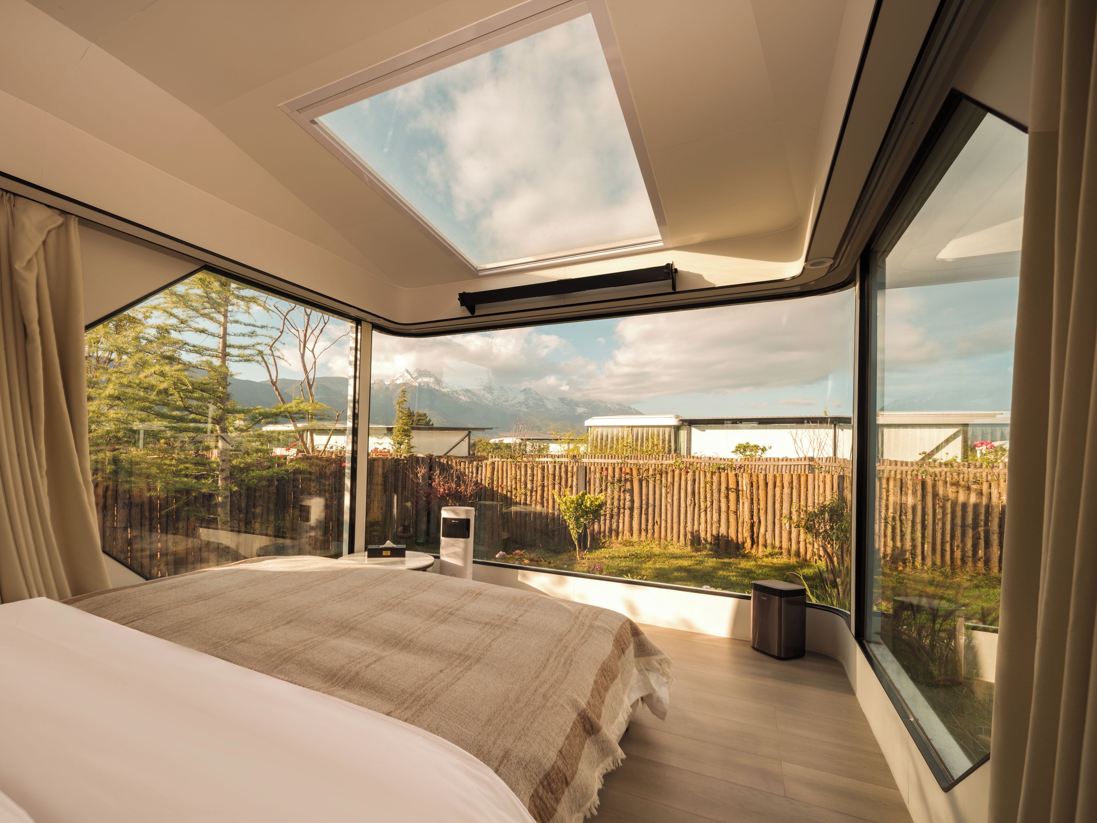 A bedroom with a large bed, a skylight, and a view of a garden and mountains.