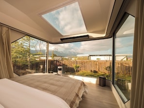 Een slaapkamer met een groot bed, dakraam en uitzicht op een tuin en bergen.