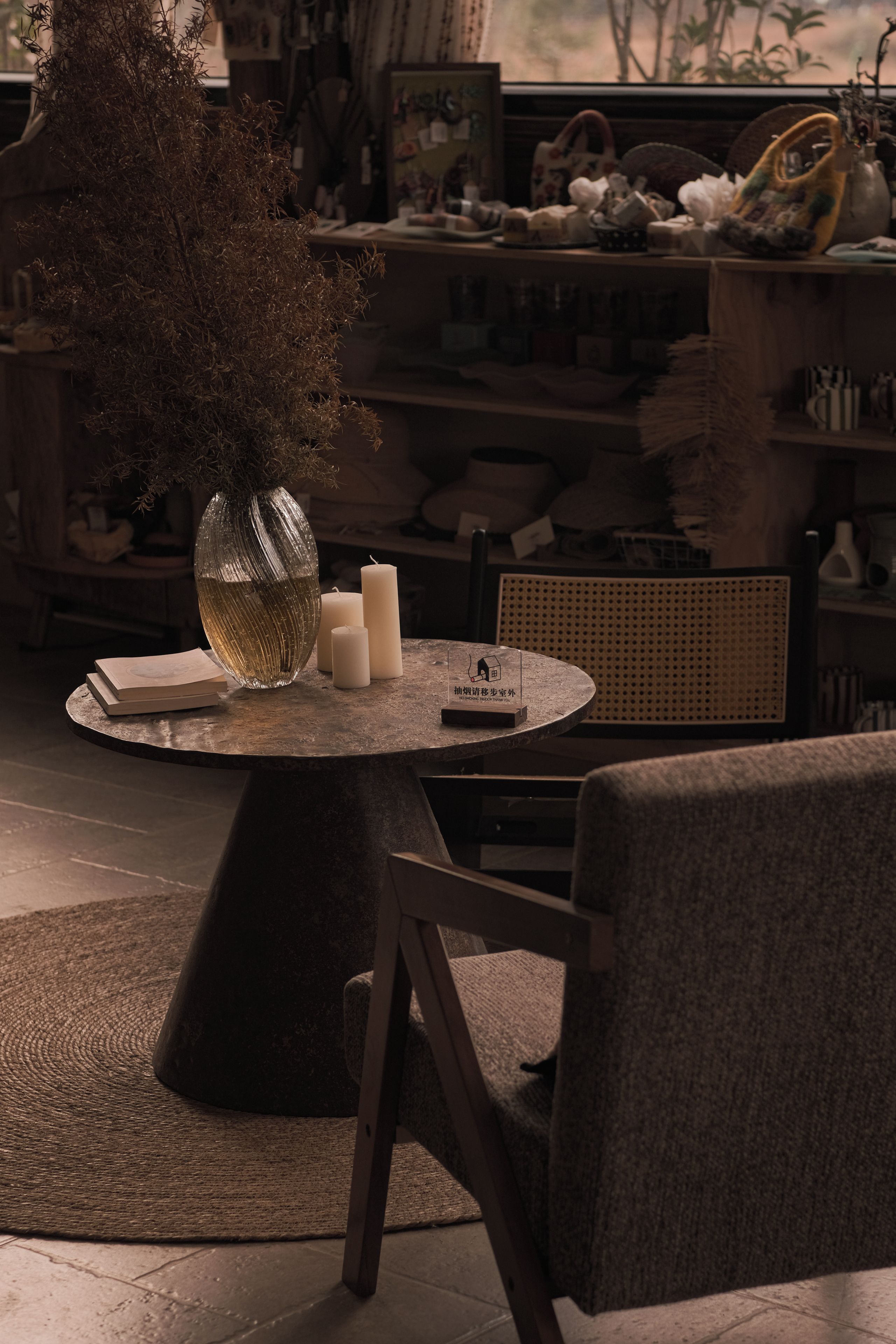 Una mesa redonda con un florero y velas, una silla y una estantería al fondo.