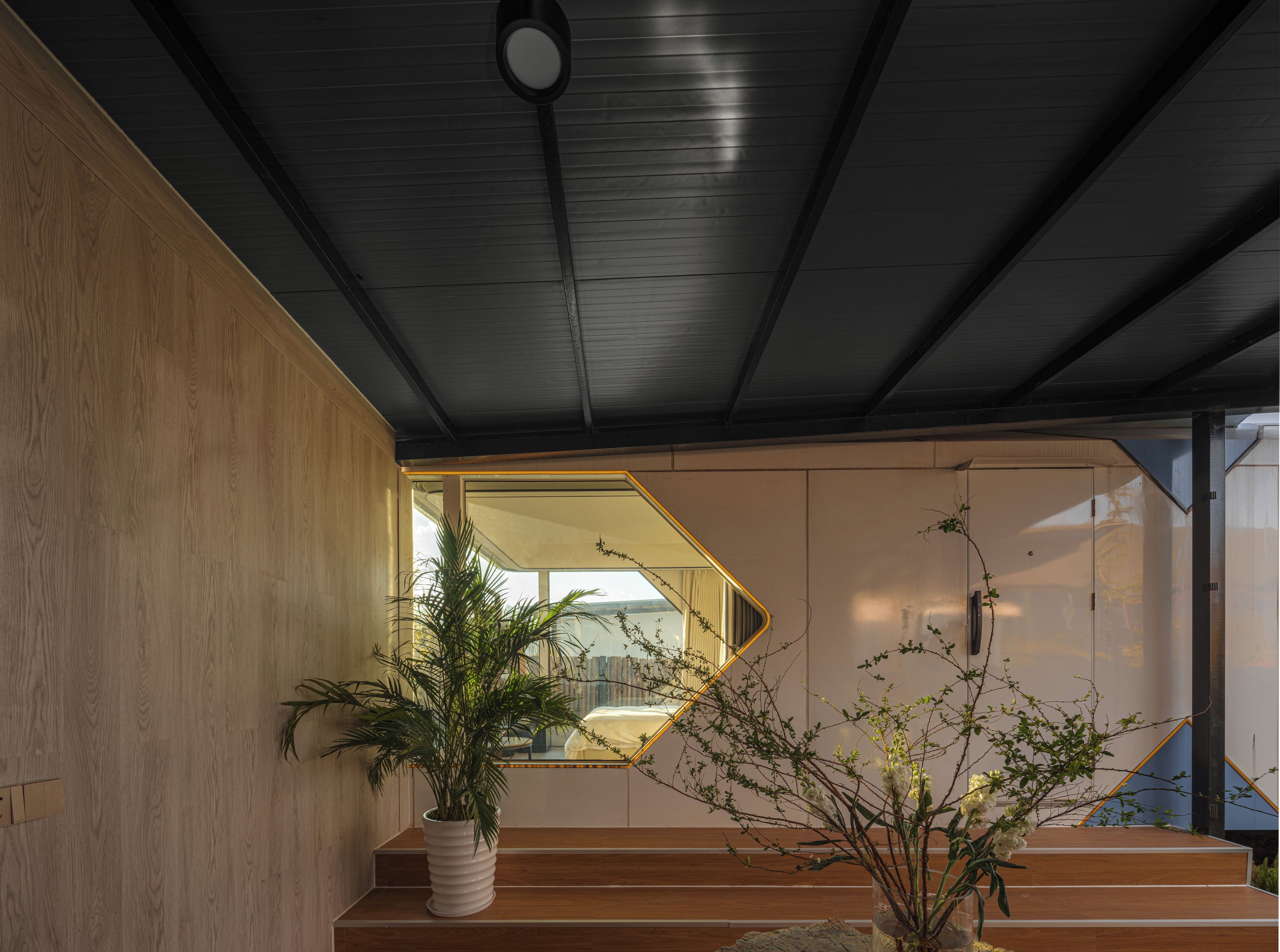 A modern interior with a staircase leading to a balcony, wooden walls, and potted plants.