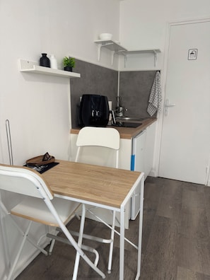 A compact kitchenette with a white chair, a small table, and a built-in sink. - Cody Studio, 25 minutes from Paris CDG, Disneyland, Paris, and the Paris Exhibition Center, (Villeparisis)
