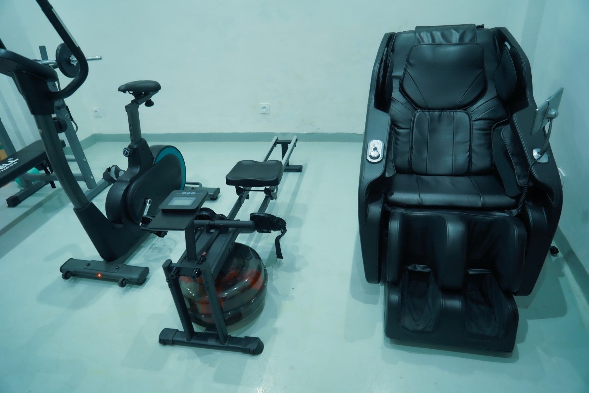 Un gimnasio con equipo de ejercicio, incluyendo una bicicleta estática, una máquina de remo y una silla de masajes.