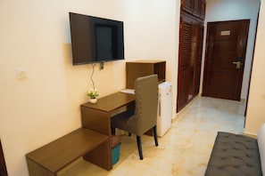 Habitación compacta con televisión de pantalla plana montada en la pared, un escritorio de madera, una silla acolchada, una pequeña planta en maceta y una puerta con un cartel de 'No Fumar'.