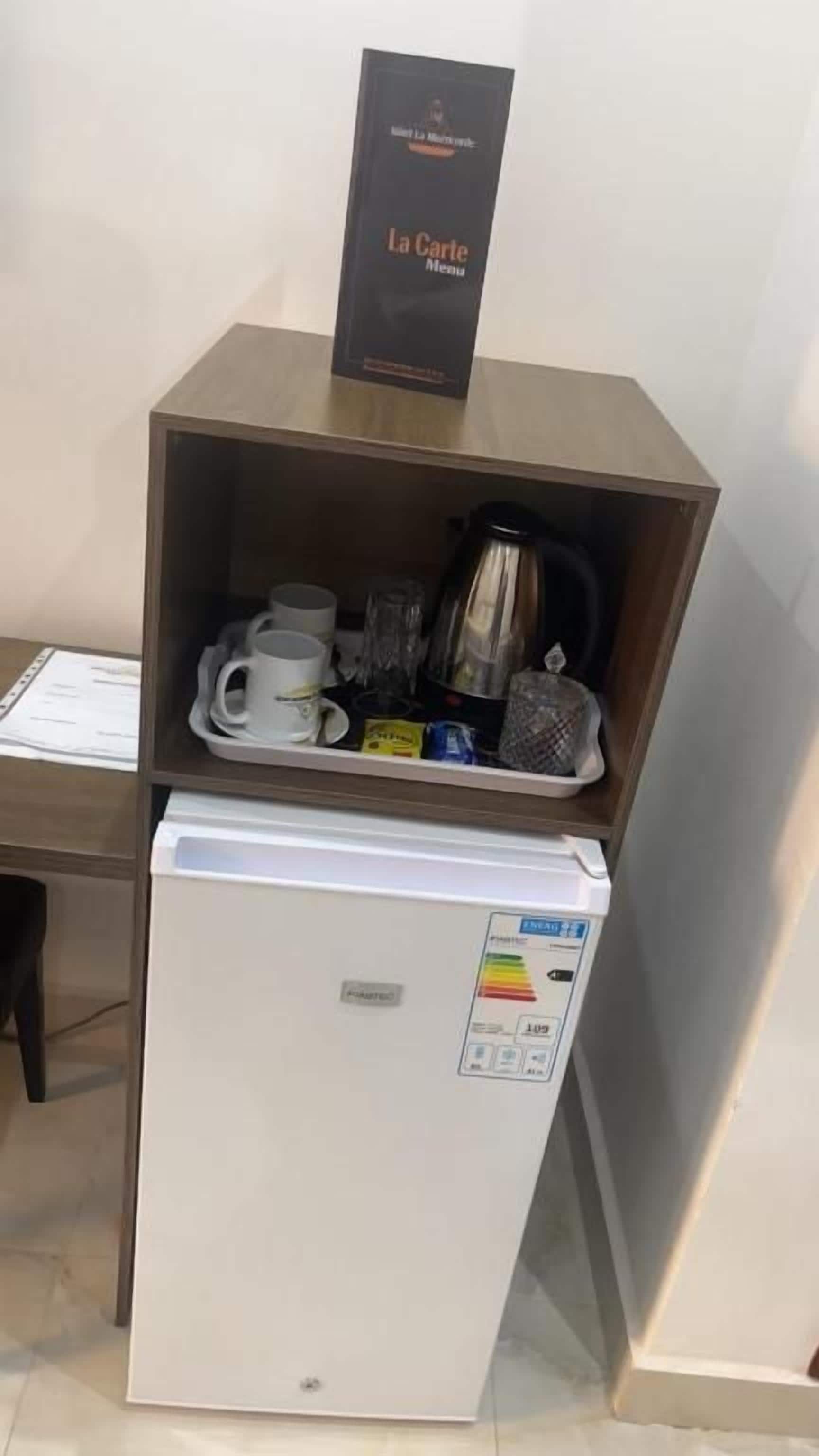 Un mini bar con una cafetera, una bandeja con tazas y una botella, y un cartel encima.