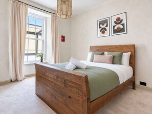 A bedroom with a wooden bed, a window with curtains, and two framed pictures on the wall. - Spacious Victorian 2BR by Leith Walk (Edinburgh)