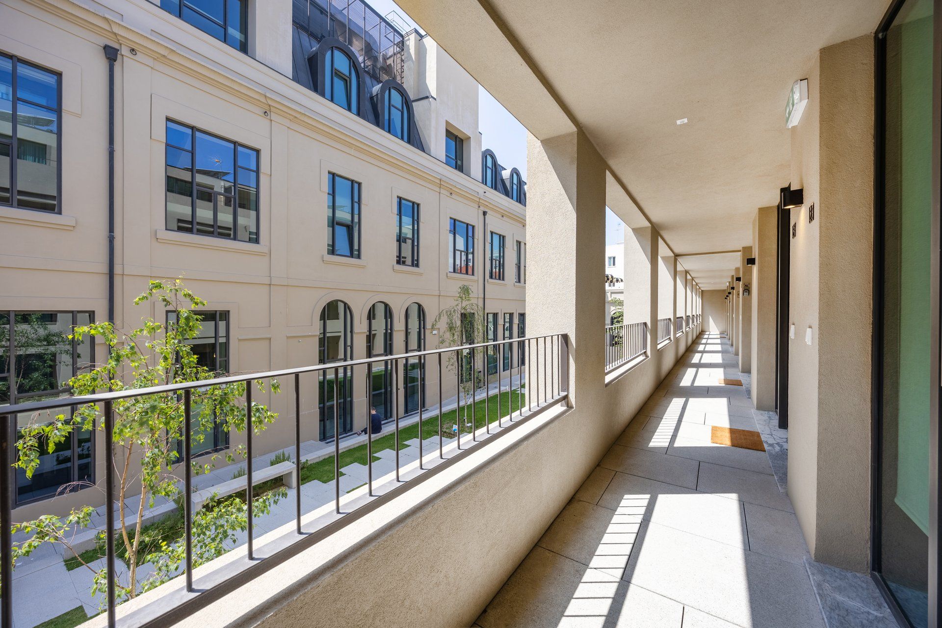 A corridor with a balcony overlooking a building with multiple windows and a clear sky.