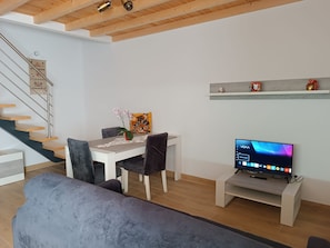Una sala de estar moderna con comedor, una escalera y un televisor sobre un mueble.