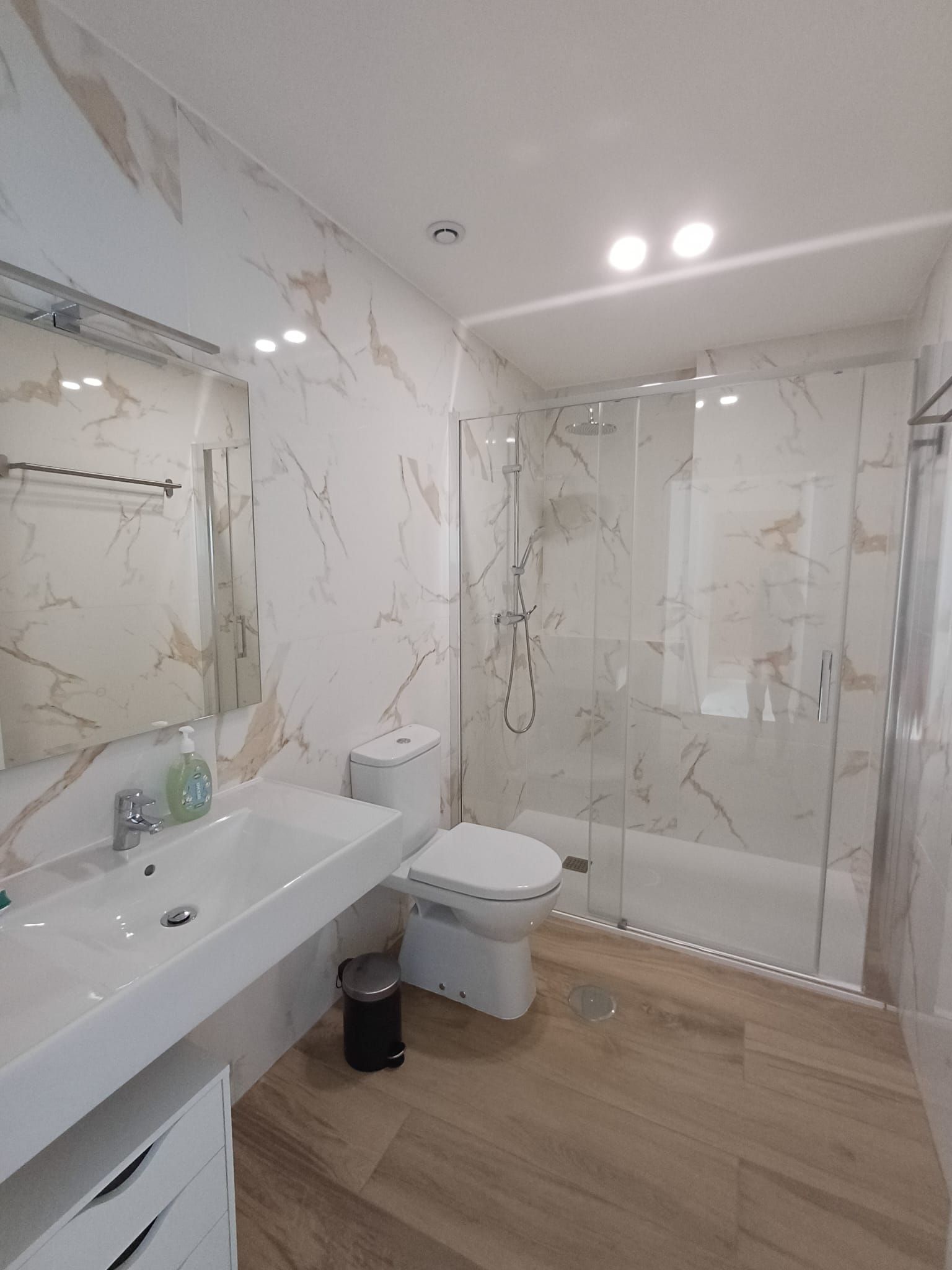 A modern bathroom with a marble backsplash, a glass-enclosed shower, a white toilet, and a large sink with a mirror.